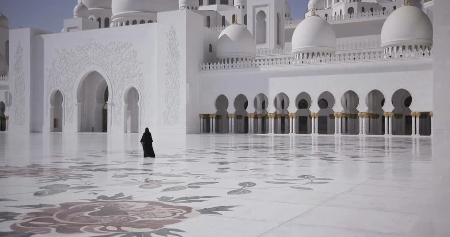 A person in a black robe is walking towards a temple