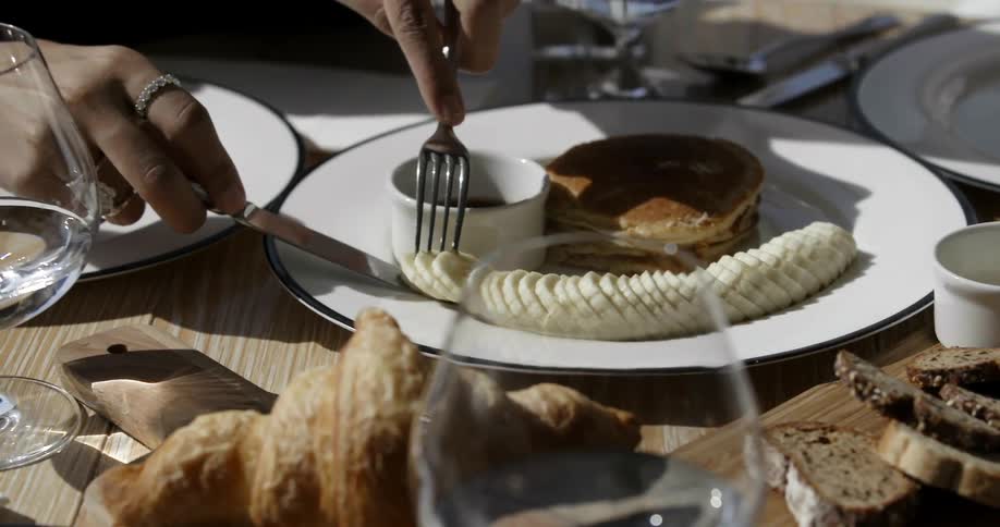 A woman eats sliced banana and pancakes