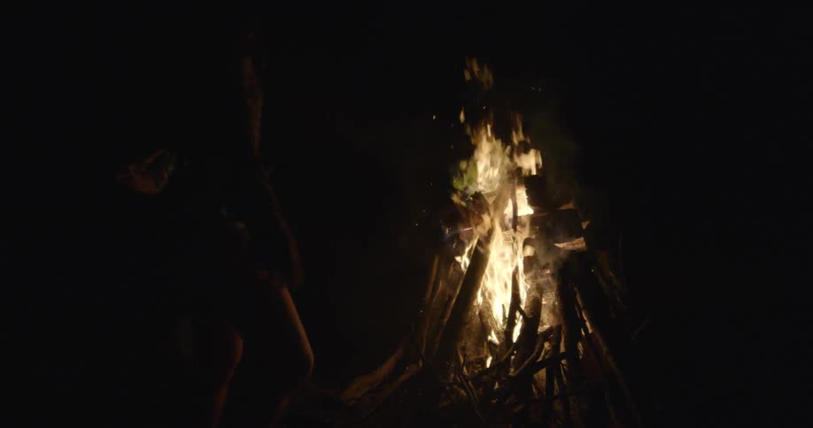 People walk around a campfire at night