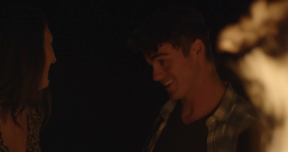 A man and woman smile and laugh near a bonfire