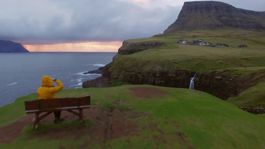 Person sits on a bench at the edge of a cliff overlooking a body of water