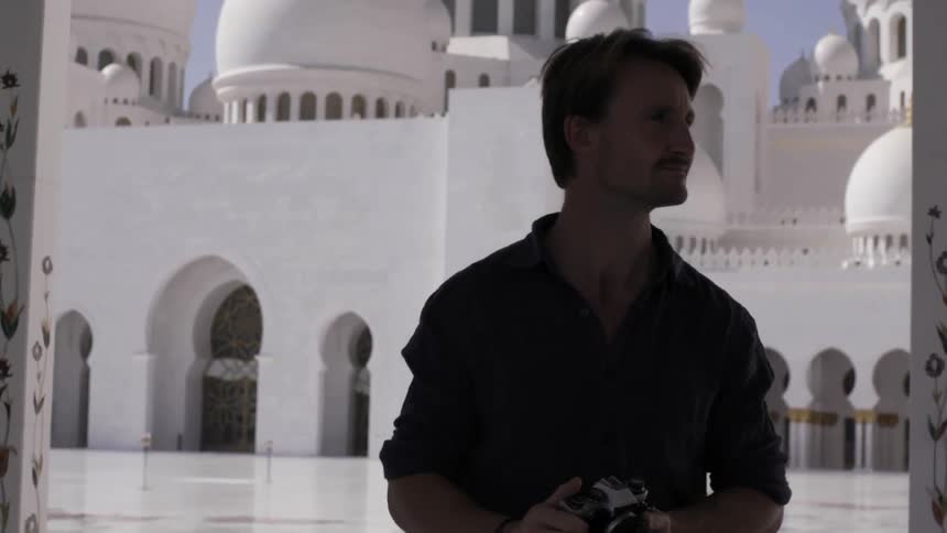 Man looks around outside of a large white building