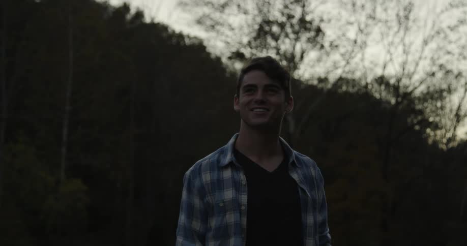 A man stands smiling in a forested area