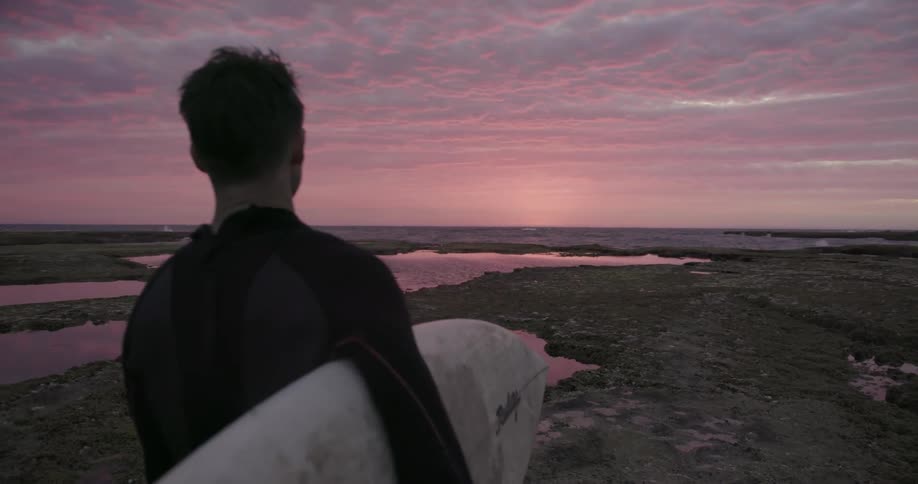 Man holding a surfboard looks out at the water