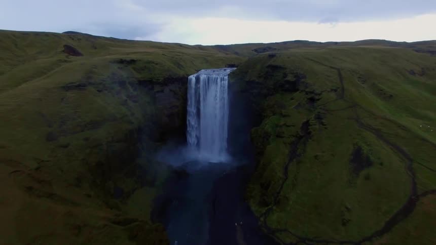 A waterfall flows over green hills into a large river
