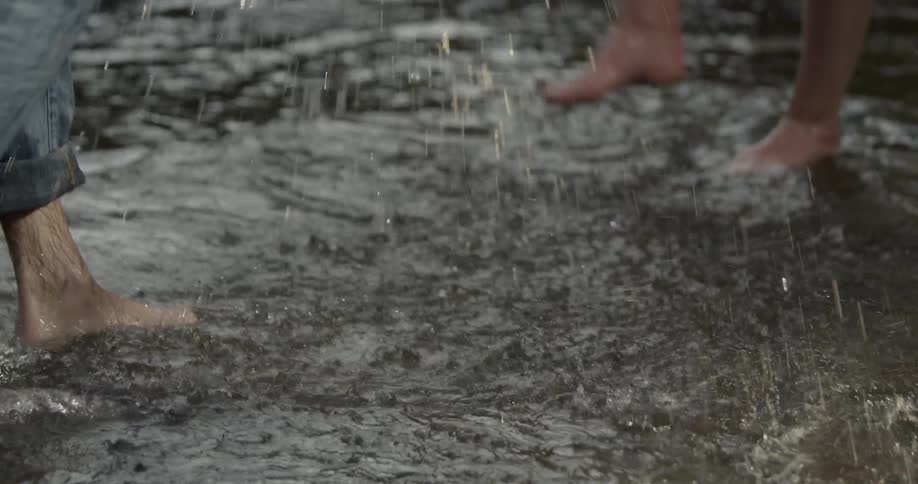 Two people kick water at each other in a creek