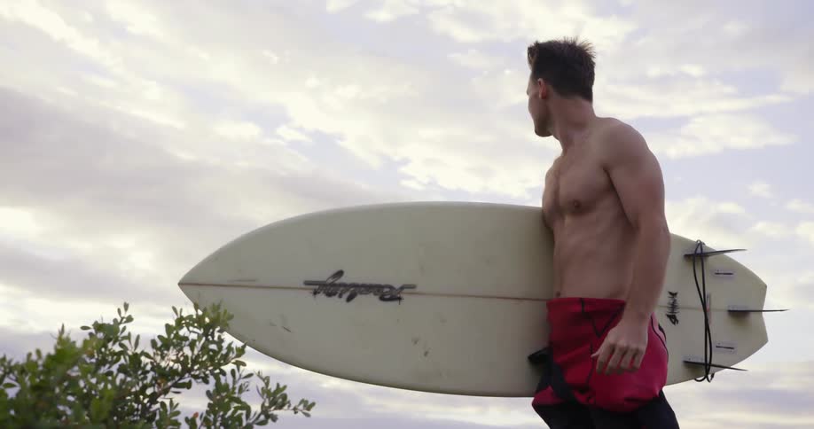 A man is walking outside carrying a surfboard