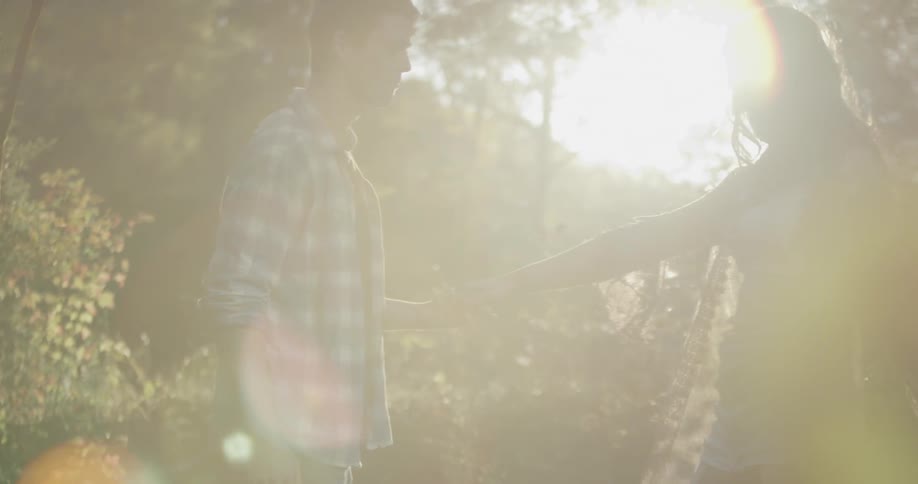 A man twirls a woman around outside on a sunny day