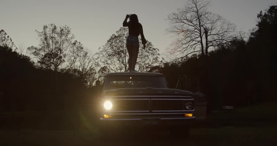 A woman dances on top of an old pickup truck