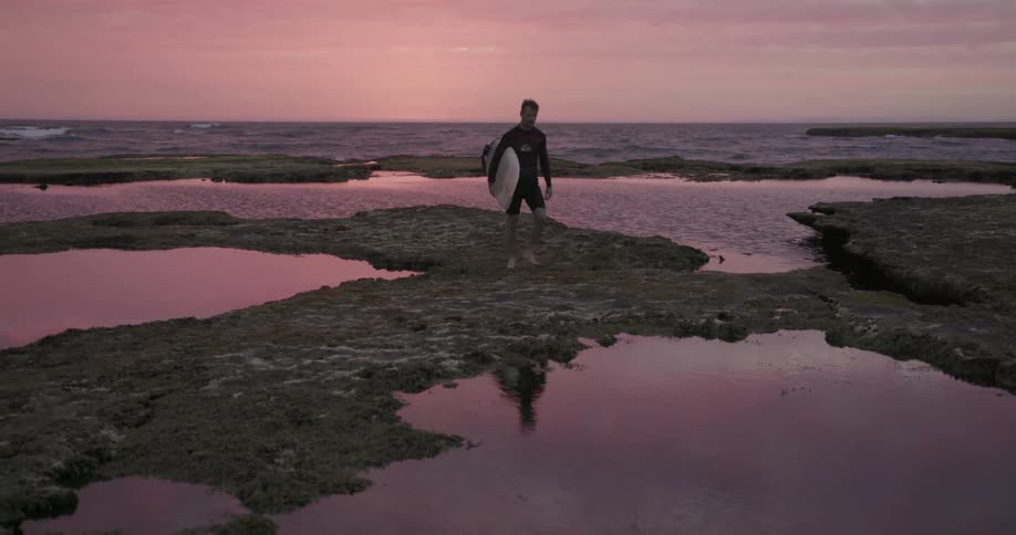 Person carrying a surfboard walks through large puddles
