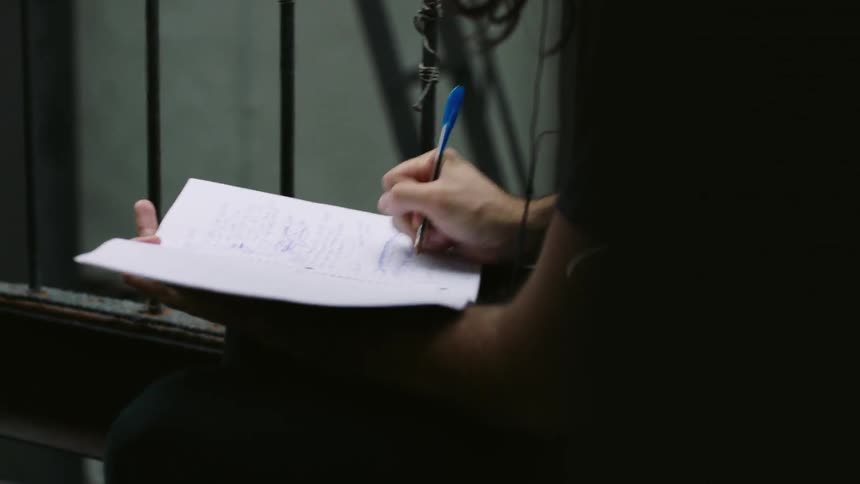 A man writes in a notebook on a balcony