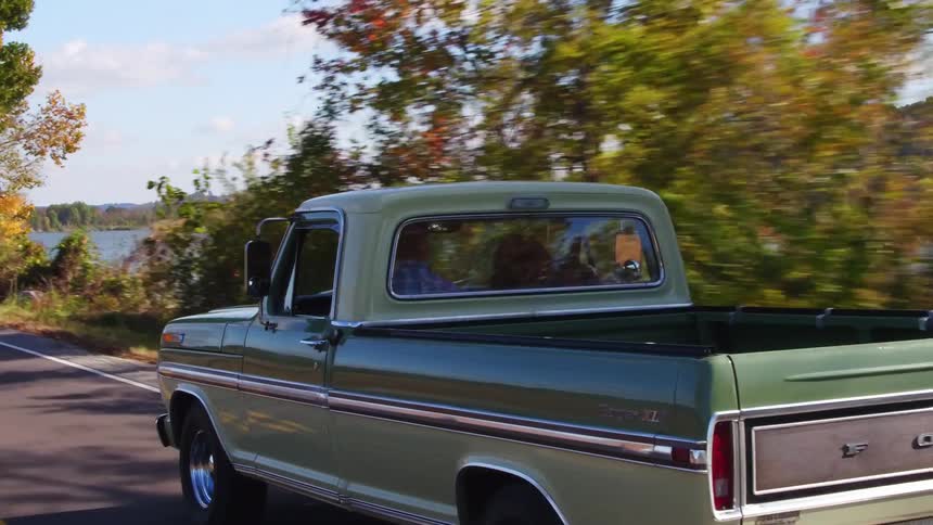 An old pickup truck drives by a lake in the fall