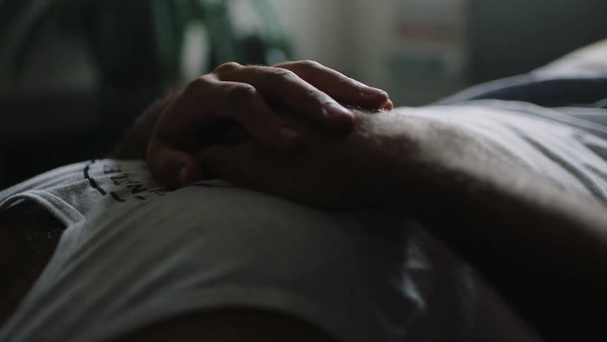 Man lays on a bed and taps his finger on his other hand