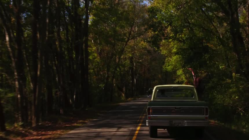 A woman leans out the passenger window of a moving pickup truck
