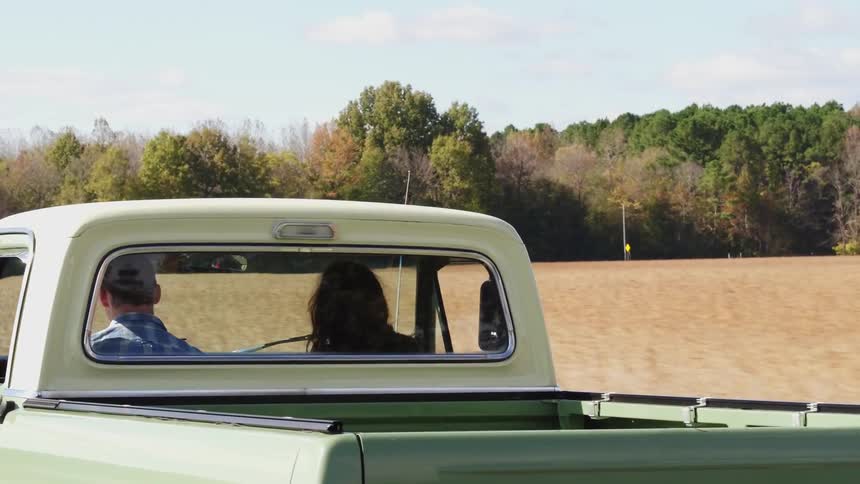 A man and woman drive down the road on a sunny day