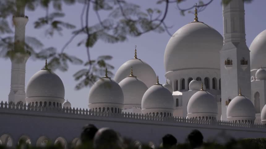People walk in front of domed buildings on a sunny day