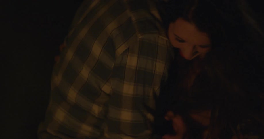 Man and woman laugh in front of a fire outside at night