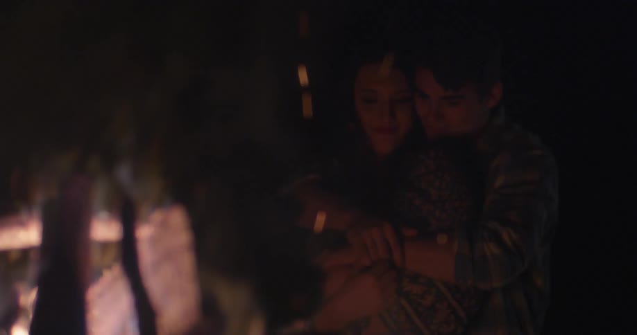 A man and woman cuddle near a bonfire