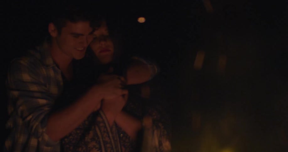 A man and woman cuddle next to a campfire