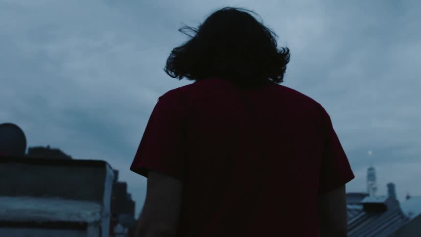 A man walks on a city rooftop at dusk