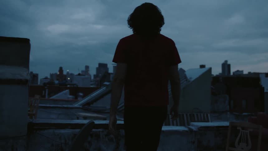 A man walking on a rooftop takes in a city view at dusk