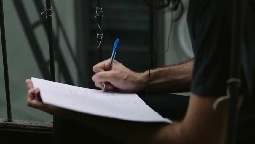 A man is writing in a notebook outside with a pen