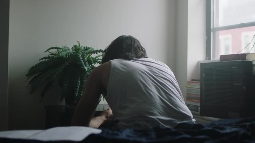 A man listens to music while sitting on a bed