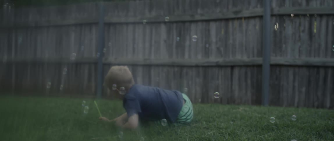 A boy rolls on the lawn with bubbles floating all around