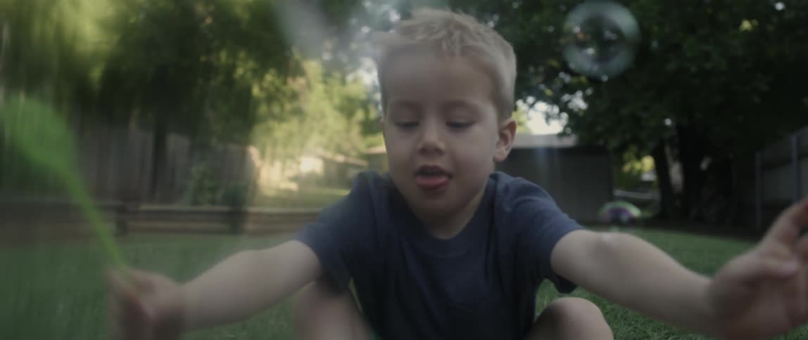 A boy plays with bubbles on a grassy lawn