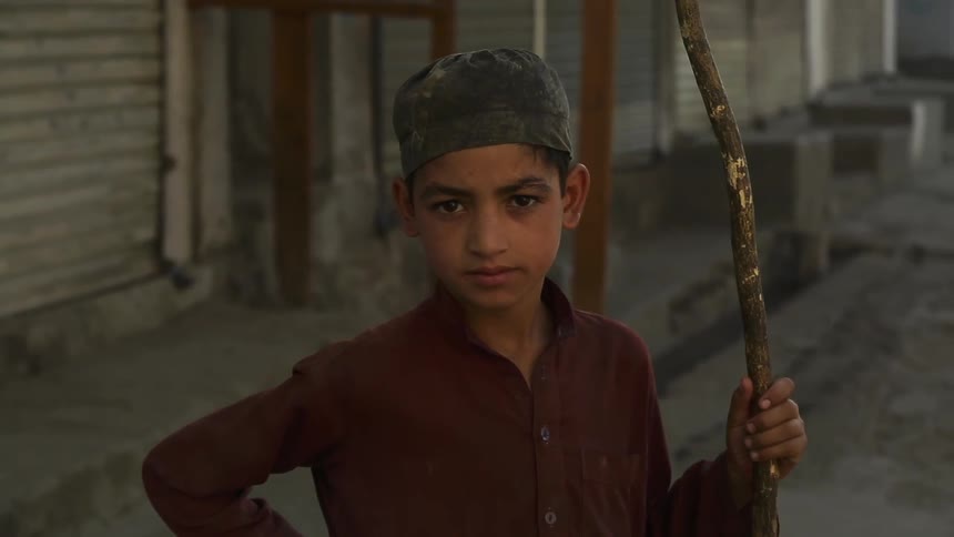 A boy holds a stick while standing on a sidewalk