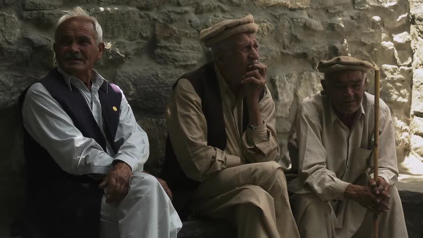 Three men sit near a rocky wall