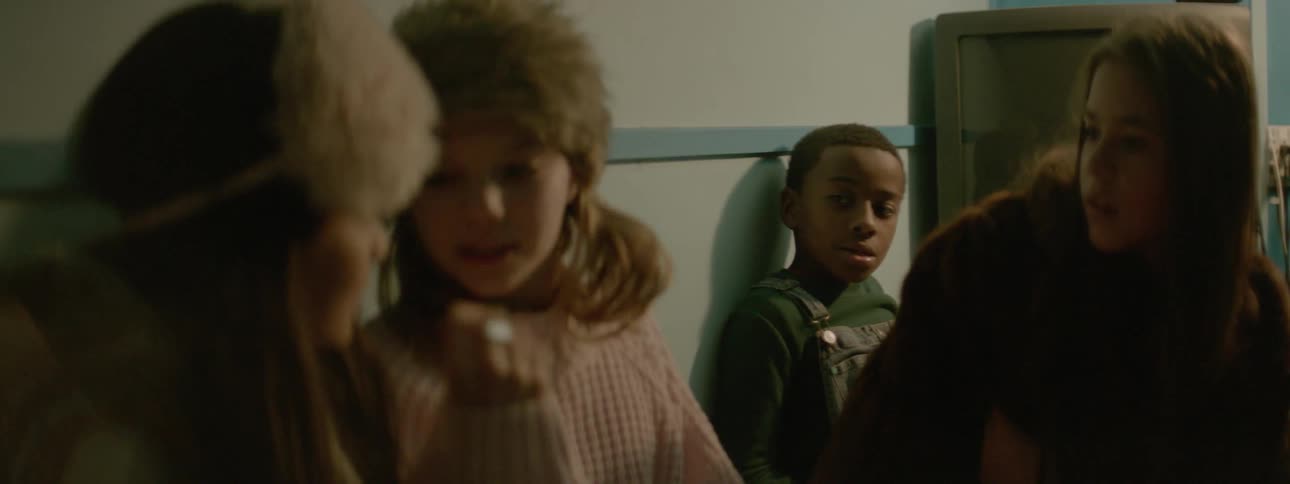 Two girls wearing fur caps sign to each other while a boy watches