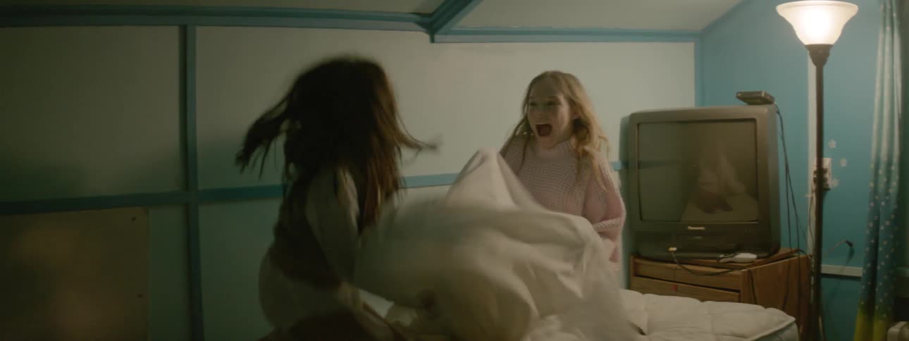 Two girls bounce on a bed and play with a sheet