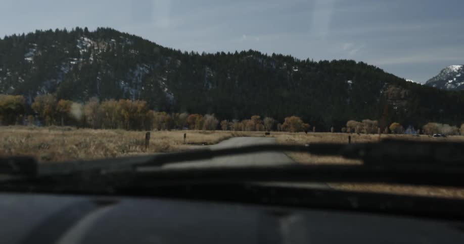 A car drives on a rural road with mountains in the distance