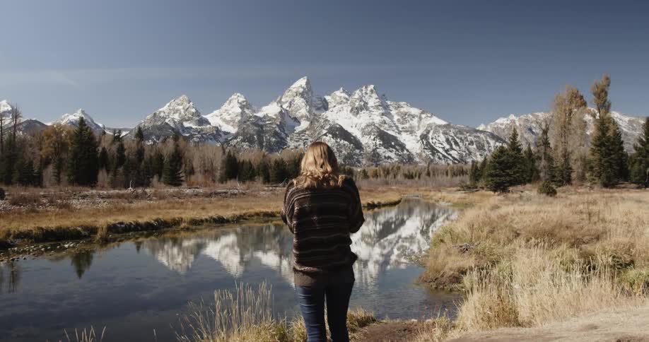 A woman takes a photo of a mountain lake on a sunny day