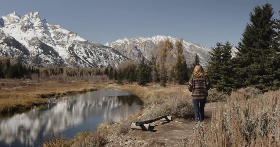 Woman takes a picture of a stream and mountains