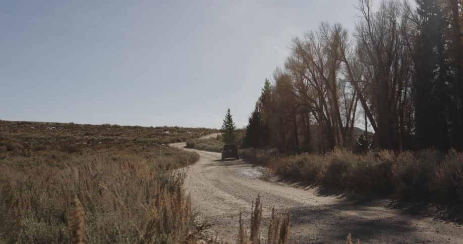 A car drives down a gravel road in the wilderness
