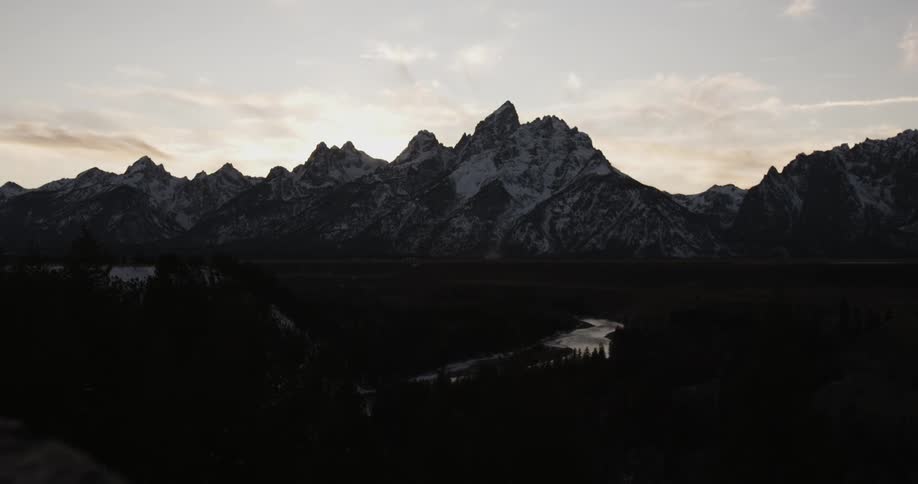 A river runs in front of snowy mountains at sunset