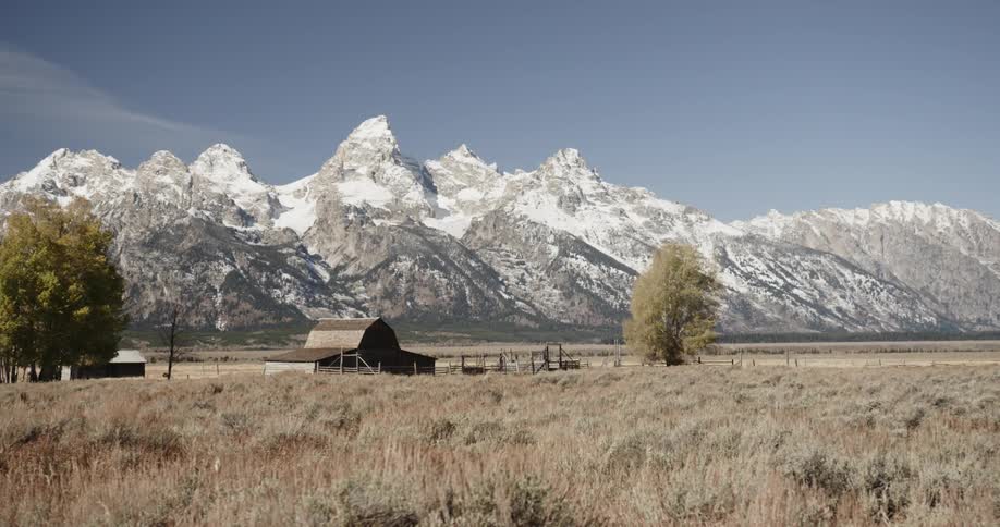 Jagged, snow capped mountains behind an old barn