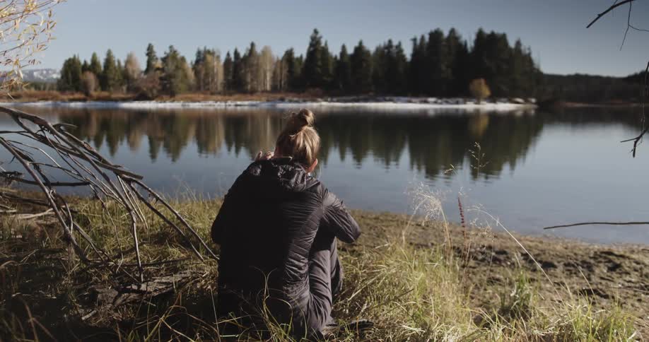 A woman is sitting by the lake taking pictures