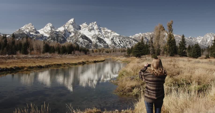 Woman takes a picture of a stream and mountains