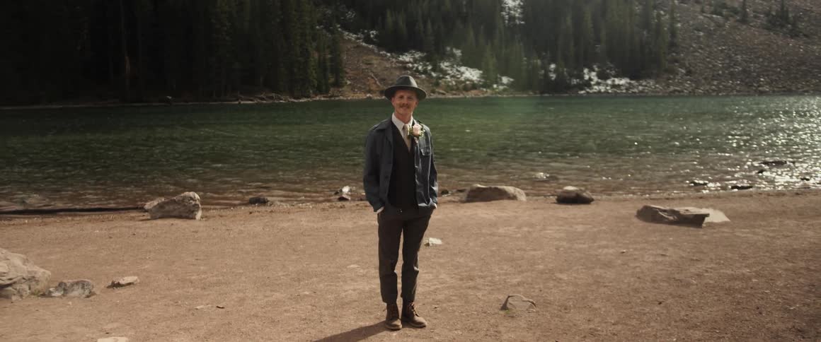 A man in a hat stands in front of a river during the day