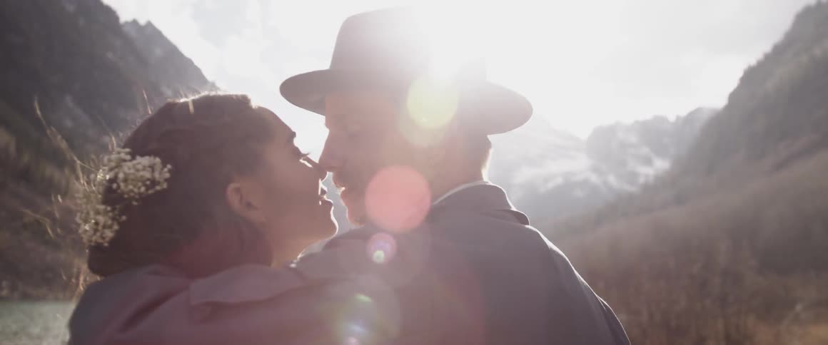 A man and woman kiss in the mountains on a sunny day