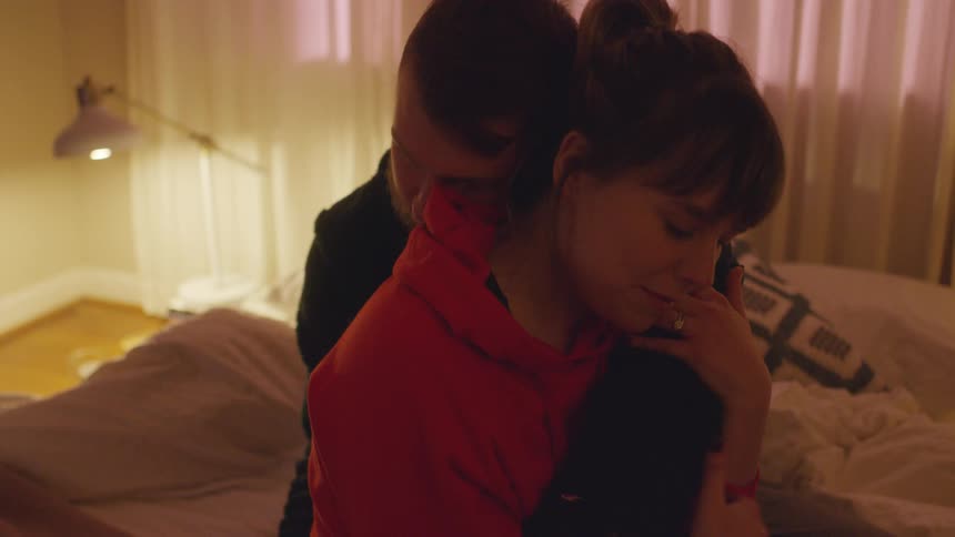 A man and woman embrace each other while sitting on a bed