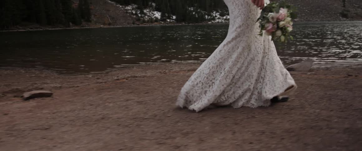 A woman wearing a wedding dress is walking by a stream