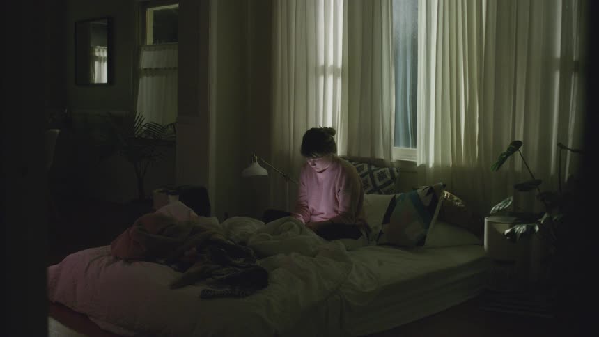 A woman sits on a bed and uses her phone