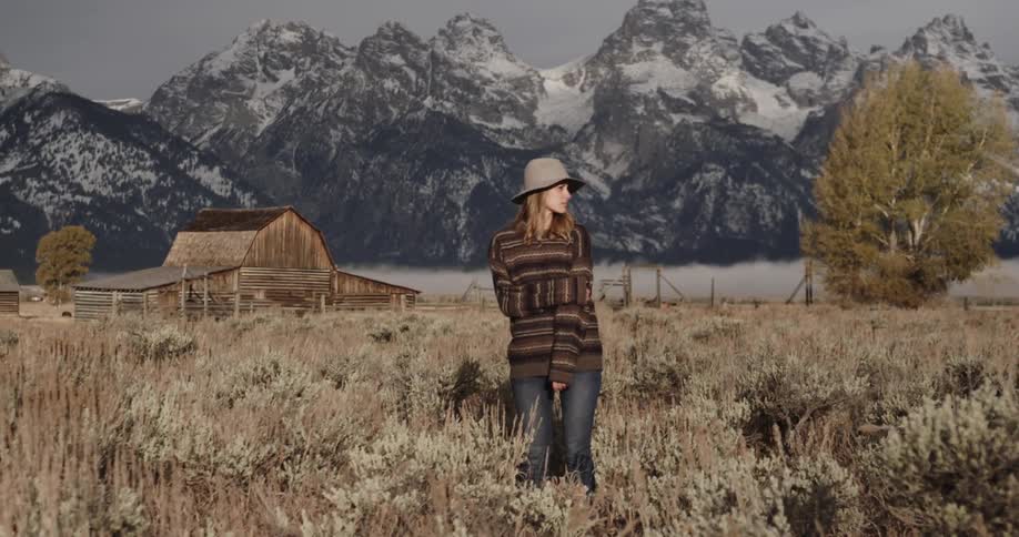 Woman standing in the middle of a field with snowy mountains in the background
