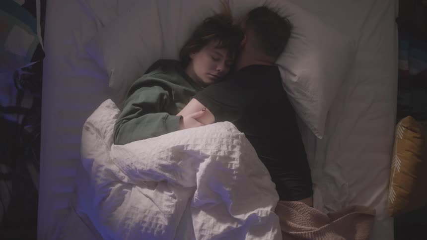 A man and woman cuddle in bed while they sleep