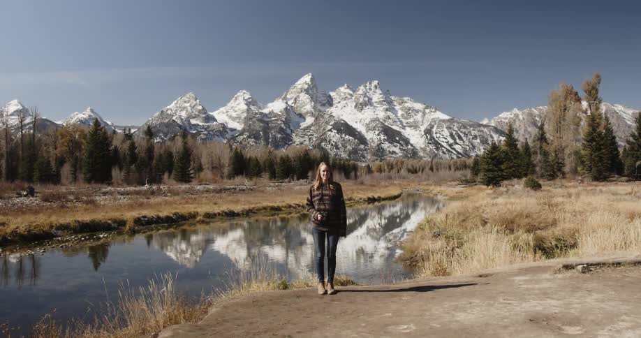 Woman standing in front of a stream and snowy mountains