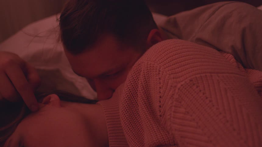 A man lovingly touches a woman's head while laying in bed